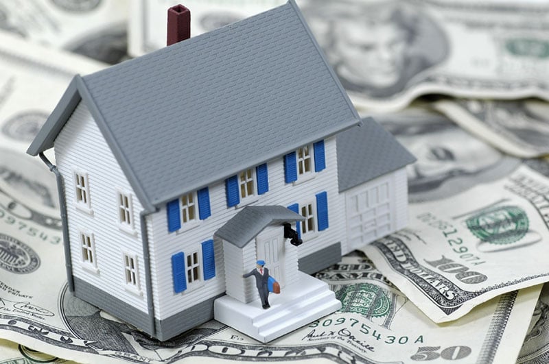 estate-planning-california-resized Plastic toy house with man standing on front porch. House is displayed on dollar bills.