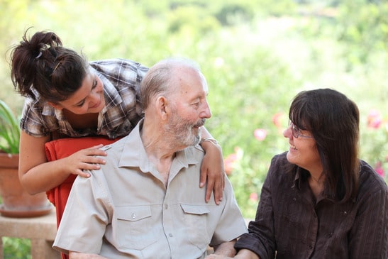 elderly man with middle aged woman and young woman sit together smiling